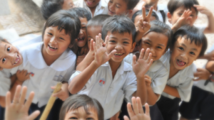 Happy school children in uniform all crowding into the frame to smile and wave.