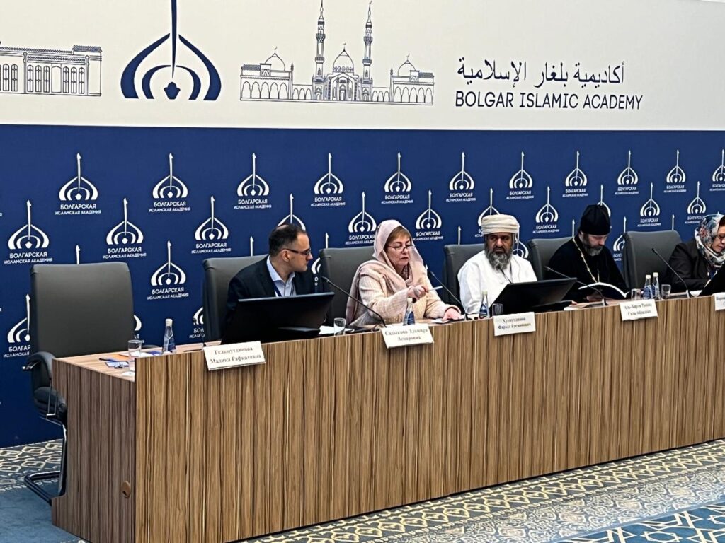 A panellists podium behind which five people are seated, two women and three men, some dressed in attire that reflects their religious beliefs. 