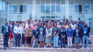 A large group of happy people standing on a set of low steps outside an impressive glass fronted building