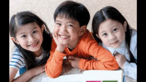 Close up from the cover of the Routledge International Handbook of Life and Values Education in Asia, featuring three cute kids with books open in front of them smiling at the camera