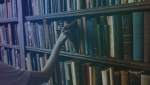 Someone talking a book from a library wall, filled with books, journals, papers and publications.